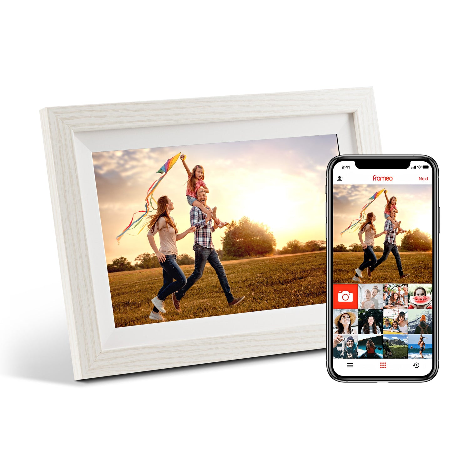 White digital photo frame displaying a photo of two children flying a kite in a sunny field, next to a smartphone showing the companion app.